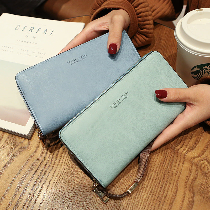 Two blue wallets held by hands on a wooden surface with a Starbucks cup in the background.