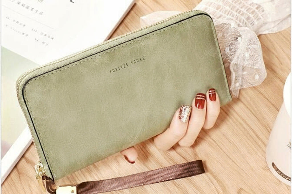 Green wallet with strap held by a hand on a wooden surface