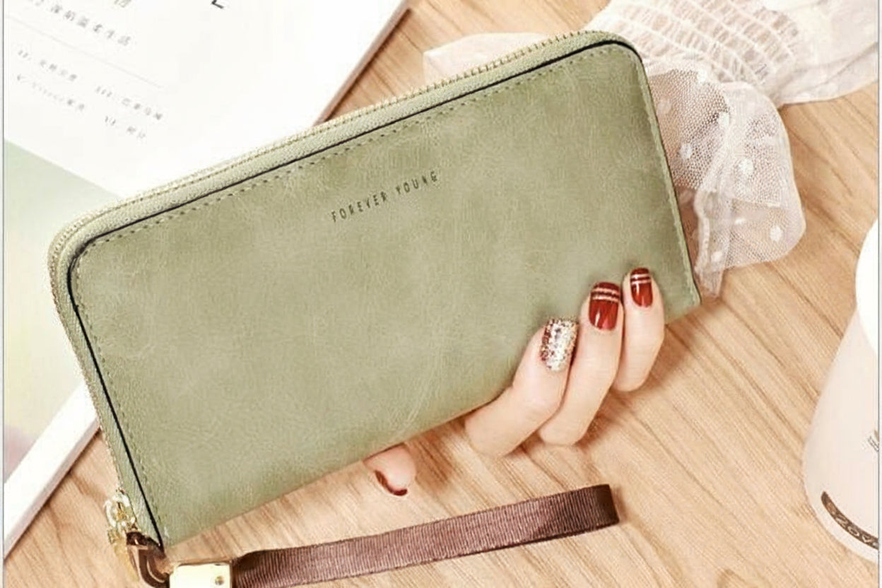 Green wallet with strap held by a hand on a wooden surface